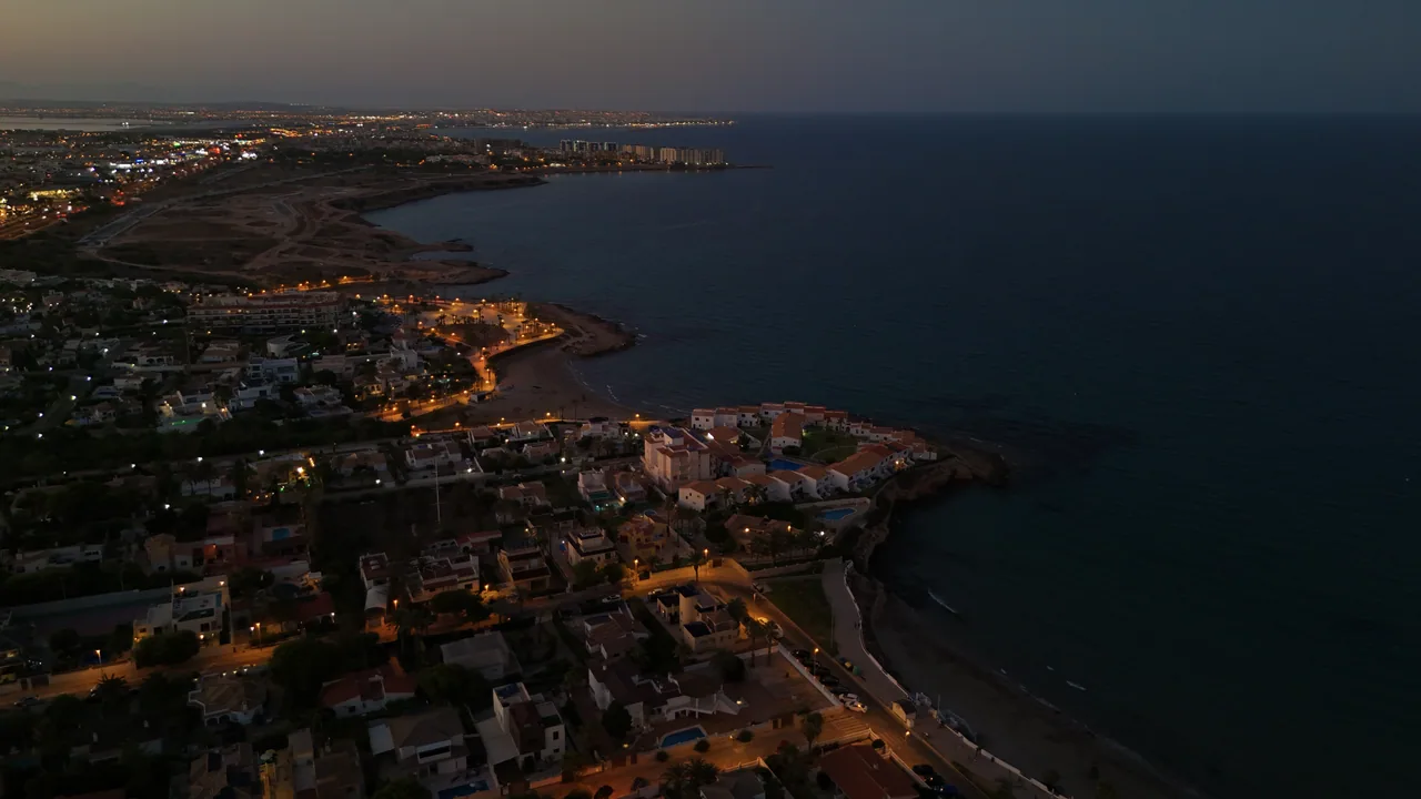 Costa con calas y luces de la ciudad al anochecer